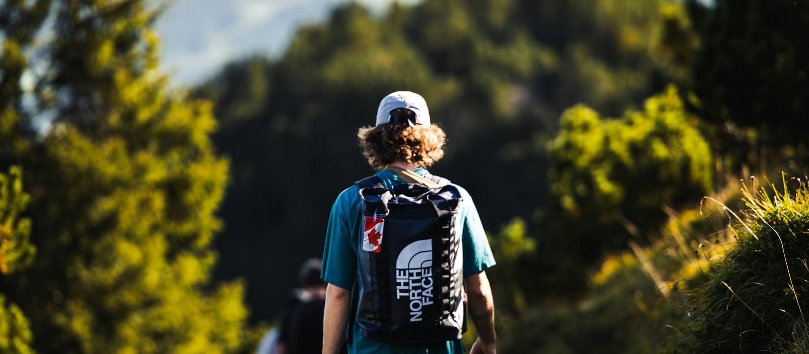 Hiker walking a forest trail toward an alpine peak