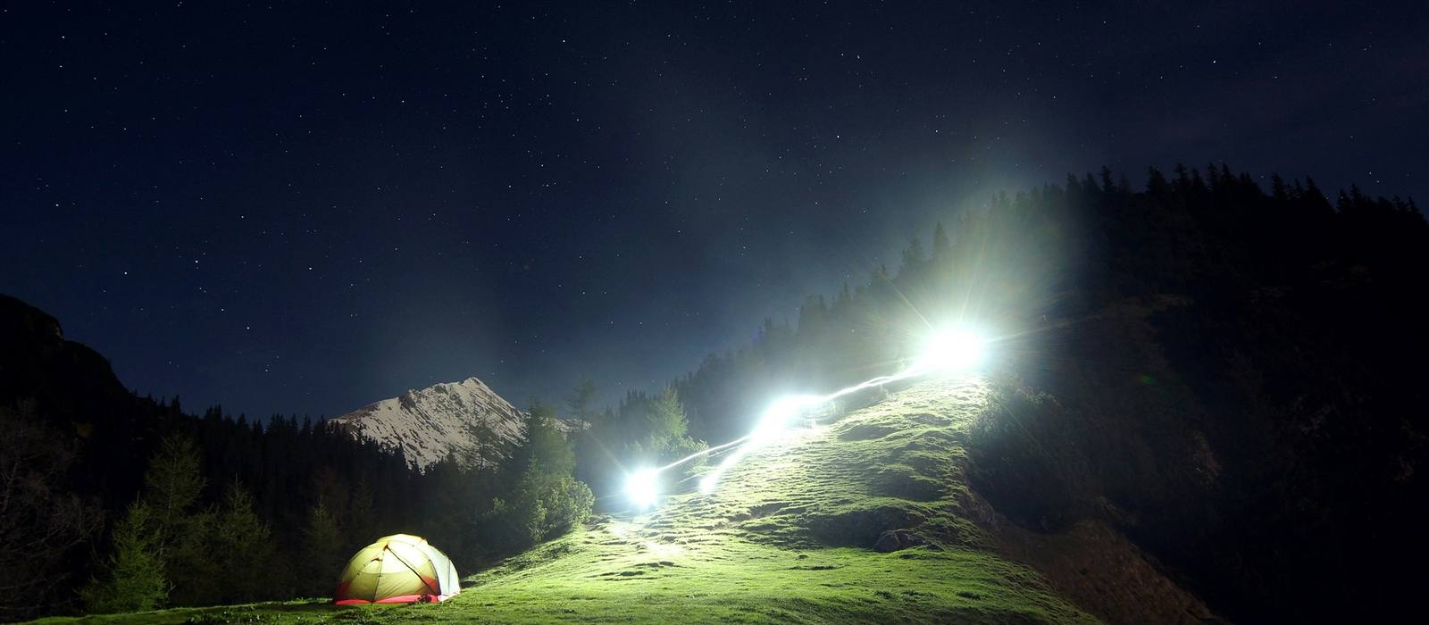 Headlamps and lights shining over a hillside camp at night