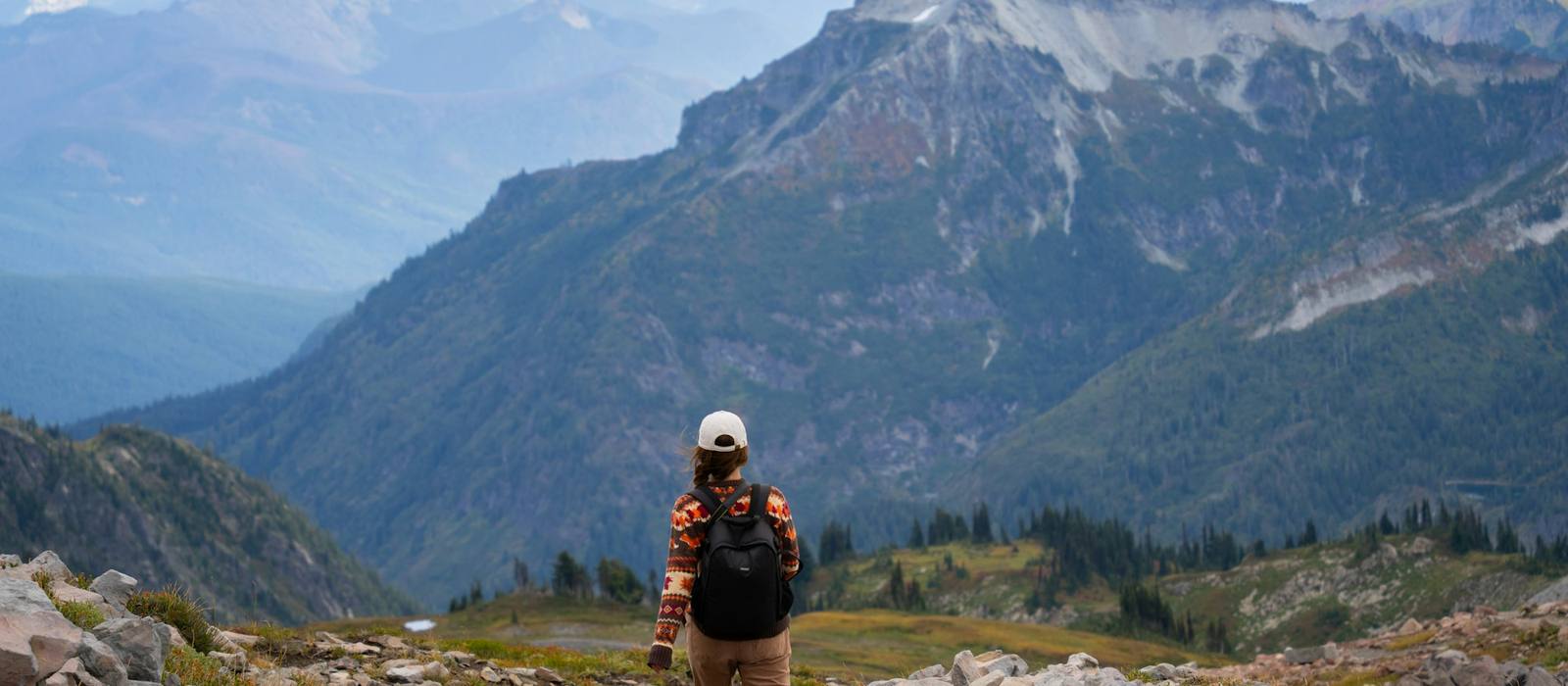 Hiker seen from behind on a rocky alpine trail facing a mountain range